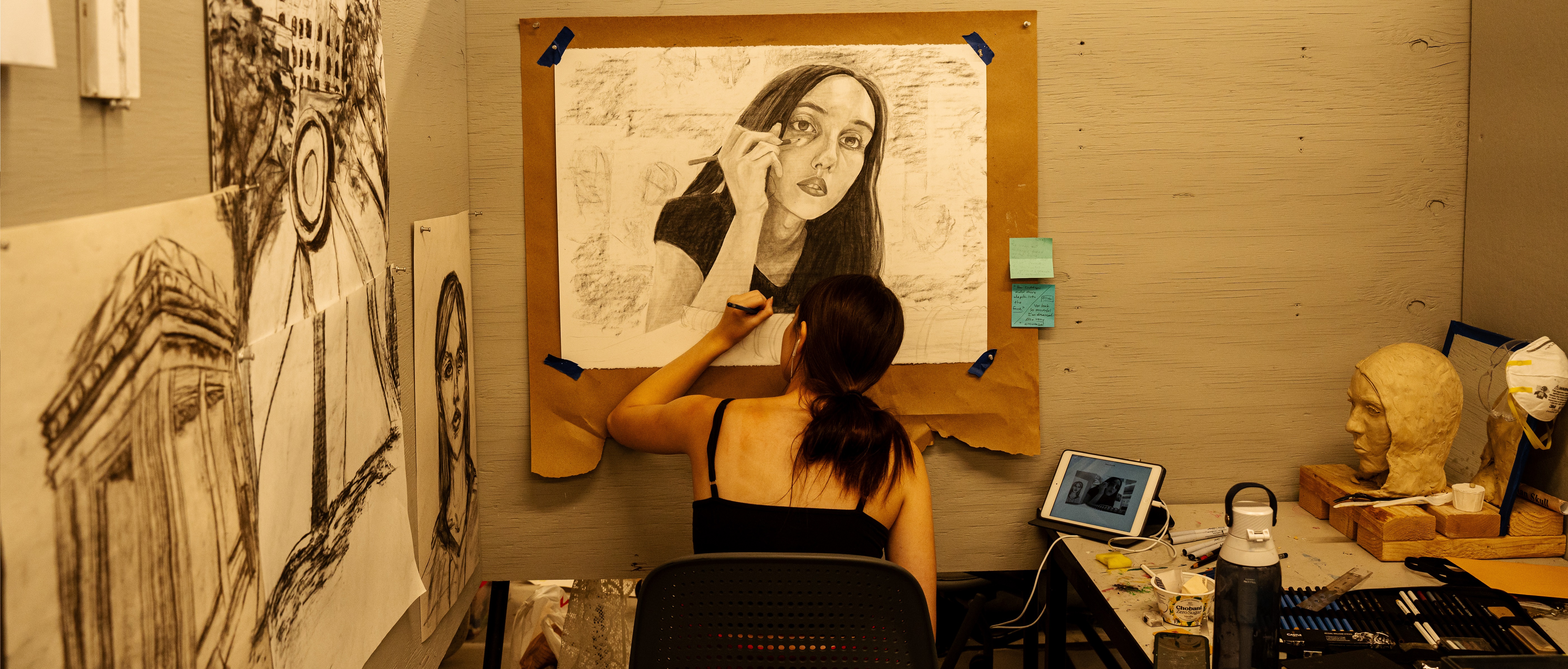 A student sits in a studio working on self-portrait in graphite. 